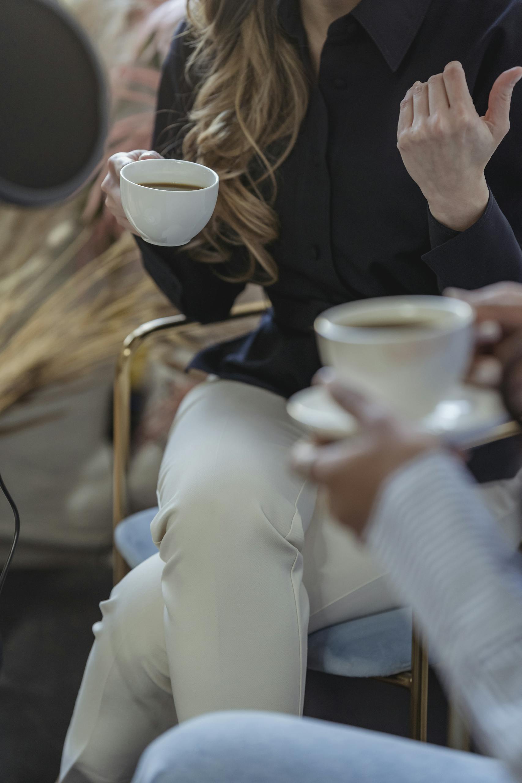 Crop anonymous female host talking to guest and having coffee while recording conversation on microphone